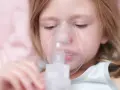 Mała dziewczynka z maską inhalacyjną na twarzy. Dziecko przechodzi inhalację na kaszel, by poczuć ulgę.