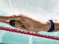 Un nageur en plein effort, profitant des bienfaits natation. La lumière joue sur son corps musclé, soulignant la puissance de ses mouvements sous l'eau.