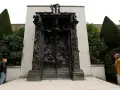 La Porte de l'Enfer de Rodin, une œuvre monumentale en bronze, se dresse au milieu d'un jardin. Deux visiteurs contemplent cette sculpture complexe.