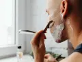 Mężczyzna goli się brzytwą pod włos, tworząc gładką skórę.