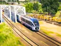 Nowoczesny pociąg PKP Intercity z niebieskim przodem mija biały most kolejowy.