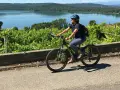 Donna in bici elettrica lungo il cammino di Oropa, tra vigneti e un lago sullo sfondo.