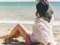 Kobieta w kapeluszu siedzi na plaży, ciesząc się spokojnymi miejscami nad morzem. Słońce i szum fal tworzą idealną atmosferę relaksu.