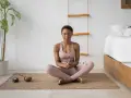Mujer meditando en postura de loto, con los ojos cerrados y un palo de incienso en las manos. A su lado, un cuenco tibetano y una vela. Aprende como meditar para encontrar la paz interior.