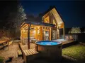 Drewniany domek z jacuzzi i tarasem, idealne miejsce na babia góra noclegi. Oświetlony girlandami, zaprasza do relaksu.