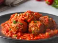 Pulpeciki w sosie pomidorowym z natką pietruszki na czarnym talerzu.