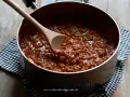 Un pentolino pieno di profumato ragù di carne, pronto per condire la pasta. Un cucchiaio di legno mescola la salsa densa e invitante.