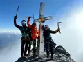 Drei Bergsteiger feiern am Gipfelkreuz des Ortler Normalwegs ihren Erfolg.