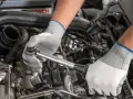 Mechanik w białych rękawiczkach dokonuje wymiany świec zapłonowych w silniku samochodu, używając klucza dynamometrycznego.