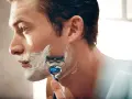 Hombre con espuma de afeitar en la cara, usando una maquinilla para afeitarse todos los días.