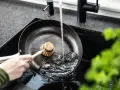 Mycie patelni żeliwnej pod bieżącą wodą za pomocą szczotki.