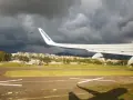 Skrzydło samolotu Ryanair nad lotniskiem, ciemne chmury na niebie.