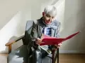 Une femme âgée, en pleine retraite, examine des documents artistiques dans un dossier rouge.