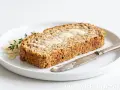 Keto chleb z mąki migdałowej i kokosowej, posmarowany masłem, na talerzu z płatkami migdałów i gałązką tymianku. Obok leży nóż.