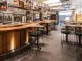 Bar moderno con taburetes verdes y mesas de madera. Un lugar ideal donde comer en Salamanca, con cocina a la vista y ambiente acogedor.