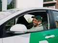 Lächelnder Mann mit grüner Kappe am Steuer eines weißen Autos mit grünen Bolt-Aufklebern. Er wird bald ein Bolt-Fahrer sein.