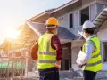 Dwóch budowlańców w kaskach i kamizelkach odblaskowych omawia postęp prac. Jeden z nich, inspektor nadzoru inwestorskiego, wskazuje kierunek.
