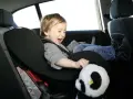 Ein fröhliches Kind sitzt im Kindersitz im Auto und spielt mit einem Panda-Stofftier.