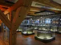 Wnętrze muzeum z zabytkowymi belkami i gablotami pełnymi artefaktów. Wśród nich można odnaleźć spichlerz błękitny baranek, symbol dawnych czasów.