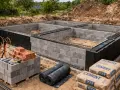 Fundamenty budynku w stanie zero. Betonowe bloki, zbrojenie i materiały budowlane, jak cement, czekają na dalsze prace.