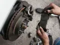 Mechanik trzyma nowe klocki hamulcowe. Sprawdź wymiana klocków hamulcowych cena i zadbaj o bezpieczeństwo.