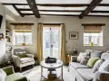 Salon confortable d'un maison cottage anglais, avec poutres apparentes, fauteuils douillets et vue sur le jardin.