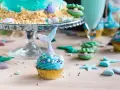 Meerjungfrau Muffins mit blauer Glasur und Schwanz-Dekorationen, umgeben von Muscheln und Seesternen.