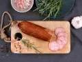 Kiełbasa żywiecka na desce, obok gałązka rozmarynu, czosnek i kolorowy pieprz. Kilka plastrów już pokrojonych.