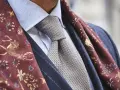 Elegancki mężczyzna w błękitnej koszuli, szarym krawacie i bordowym szalu z motywem jeleni. Całość emanuje nonszalancką elegancją, czyli sprezzaturą.