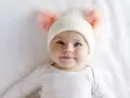 Ein süßes Baby mit blauen Augen und einer Mütze mit Bommeln. Man fragt sich, welche Augenfarbe bekommt mein Kind.