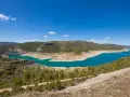 El pantano de Sacedón, con su agua turquesa, se extiende entre colinas verdes bajo un cielo azul.