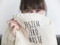 Sylwia Majcher, z uśmiechem ukrytym za torbą z napisem "Jestem Zero Waste", pokazuje swoje zaangażowanie w ekologię.