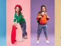 Cztery dziewczynki w modnych stylizacjach. Jedna w żółtym sweterku, druga z deskorolką, trzecia z plecakiem, czwarta w pomarańczowej kurtce. Rozmiar 122 pasuje na wiek ok. 6-7 lat.