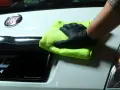 Ręka w czarnej rękawiczce z zieloną mikrofibrą czyści biały lakier Fiata. Idealne rozwiązanie, czym odtłuścić lakier przed polerowaniem.