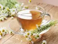 Une tasse de tisane de camomille, idéale pour le rhume traitement, entourée de fleurs fraîches sur un fond en bois.