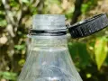 Nakrętki od butelek są przytwierdzone, by zapobiec ich zgubieniu i ułatwić ponowne zakręcenie. Widoczny fragment plastikowej butelki z otwartą, czarną nakrętką.