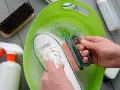 Come lavare le Superga bianche: una scarpa immersa in acqua saponata, mentre una mano la strofina con una spazzola.