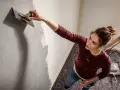 Frau trägt mit einem Spachtel eine Struktur auf die Wand auf. Die Spachteltechnik Wand verleiht dem Raum eine besondere Optik.