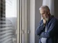 Starszy mężczyzna z siwą brodą, zamyślony, z ręką podpartą na brodzie. Wzdychający oddech, objawy smutku.