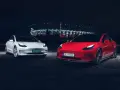 Dwa modele Tesla, biały i czerwony, zaparkowane nocą przed oświetlonym stadionem.