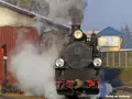 Parowozownia Wolsztyn zwiedzanie: parowóz z maszynistą w kabinie, otoczony parą, gotowy do podróży.