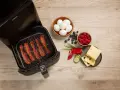 Knuspriger Bacon im Airfryer, daneben Eier, Beeren, Käse und Gemüse für ein perfektes Frühstück.