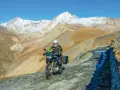 Un motociclista avventuroso affronta un sentiero impervio con la sua jafferau moto, circondato da maestose montagne innevate e paesaggi aridi.
