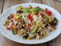 Un piatto colorato di insalata di riso vegetariana con zucchine, melanzane, pomodori e mais, guarnito con basilico fresco.