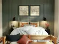 Elegantes dormitorios pequeños con encanto. Cama dorada con ropa blanca, dos cuadros de ciudades y lámparas negras.