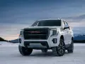 Biały GMC Yukon XL gotowy na zimową przygodę na ośnieżonej drodze, z górami w tle.
