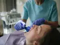 Dentysta w rękawiczkach zakłada pacjentowi niebieski retraktor jamy ustnej.