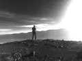 Ein Mann steht auf einem felsigen Gipfel und blickt in die Ferne. Die Sonne bricht durch die Wolken und beleuchtet die Berge. Vielleicht fragt er sich, was ist Weisheit.