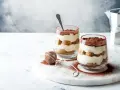 Dwa pucharki z kremowym tiramisu bez jajek, posypane kakao. Obok sitko do kakao i kawiarka.