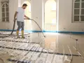 Operaio versa materiale autolivellante su pavimento esistente con riscaldamento a pavimento.